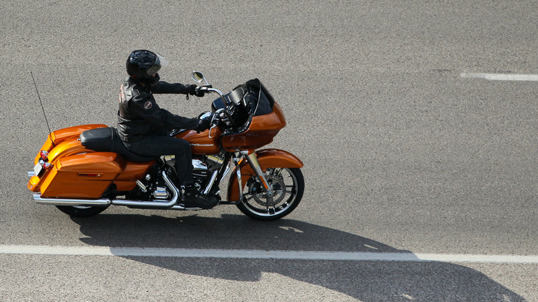 A rider in full kit riding a Harley-Davidson Road Glide finished in Amber Whisky down a road.