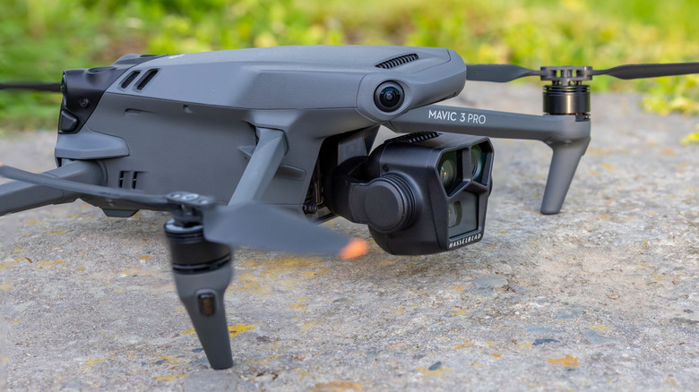 Picture of the DJI Mavic 3 Pro sitting on top of a rough surface with greenery in the background