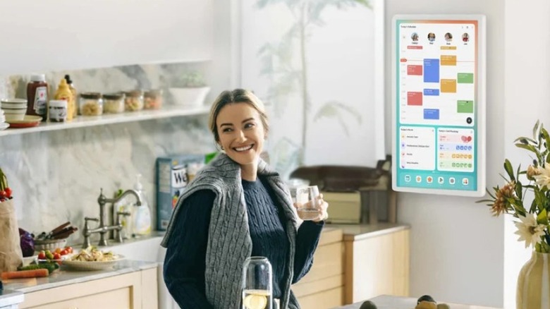 Woman drinking wine in kitchen with a digital monitor on the wall