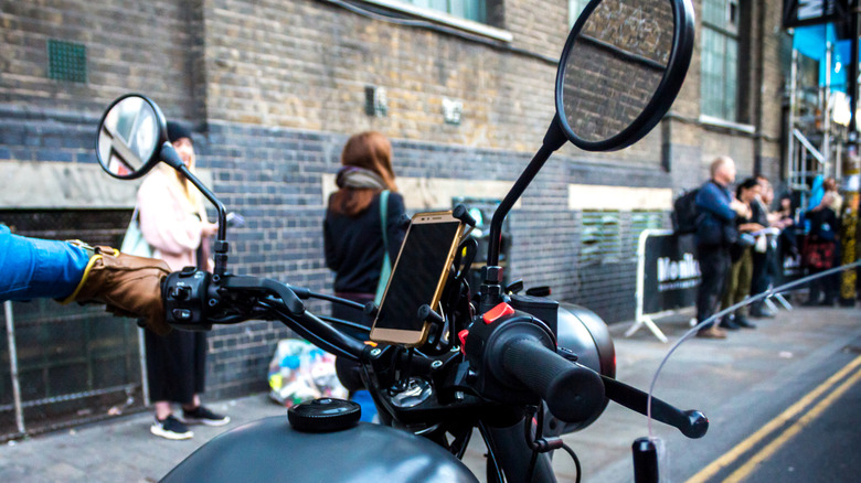 A smartphone mounted on the handlebars of a vintage motorcycle.
