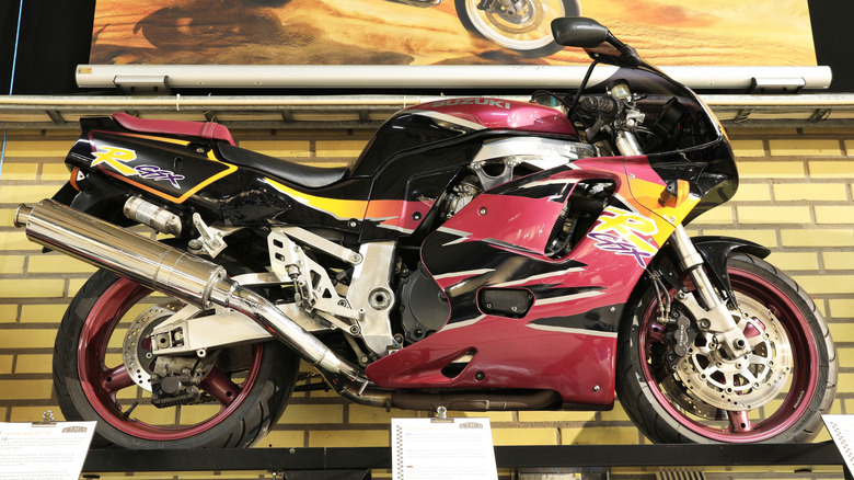A red and black 1985 Suzuki GSX-R 750 motorbike on display indoors on a podium.