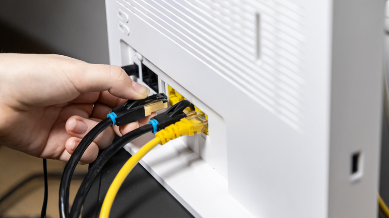 Up-close shot of an adult hand actively connecting a vital black Ethernet LAN network cable into a white Wi-Fi router