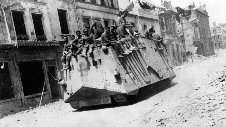A dozen soldiers ride atop an A7V through rubble of war torn city streets