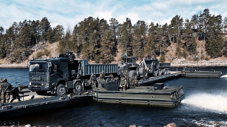 Servicemembers move heavy equipment across an erected Improved Ribbon Bridge