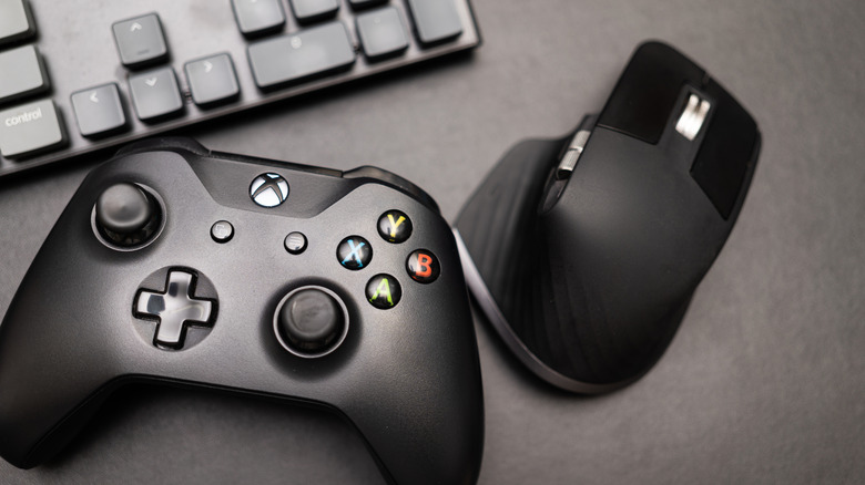 A black Xbox controller sitting next to a black computer keyboard and a black wireless mouse