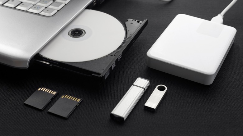 an optical drive on a laptop, an external hard drive, flash drives, and SD cards pictured together