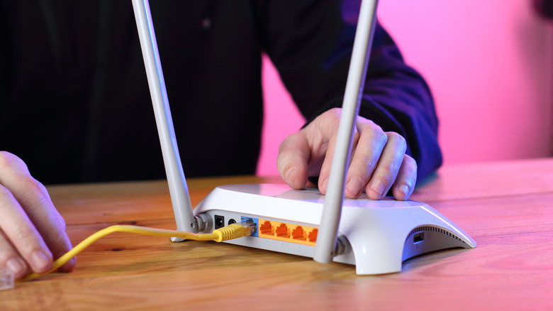 Hand on white router with yellow LAN connected