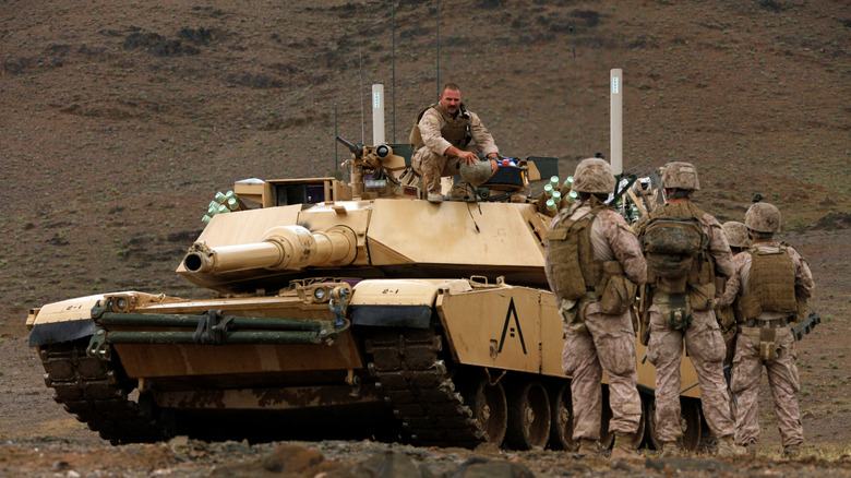 US Army soldiers stand near an M1 Abrams tank with another solider perched on top of it