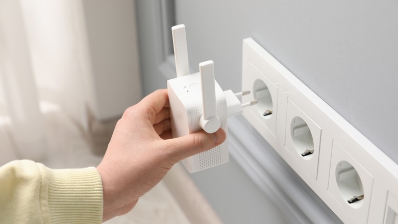 A close up of a woman inserting a Wi-Fi extender into an outlet indoors