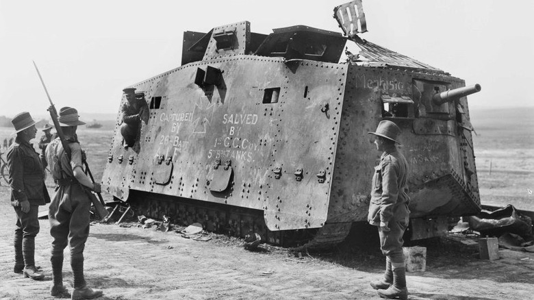 Black and white, three soldiers stand around a partly dismantled captured A7V tank